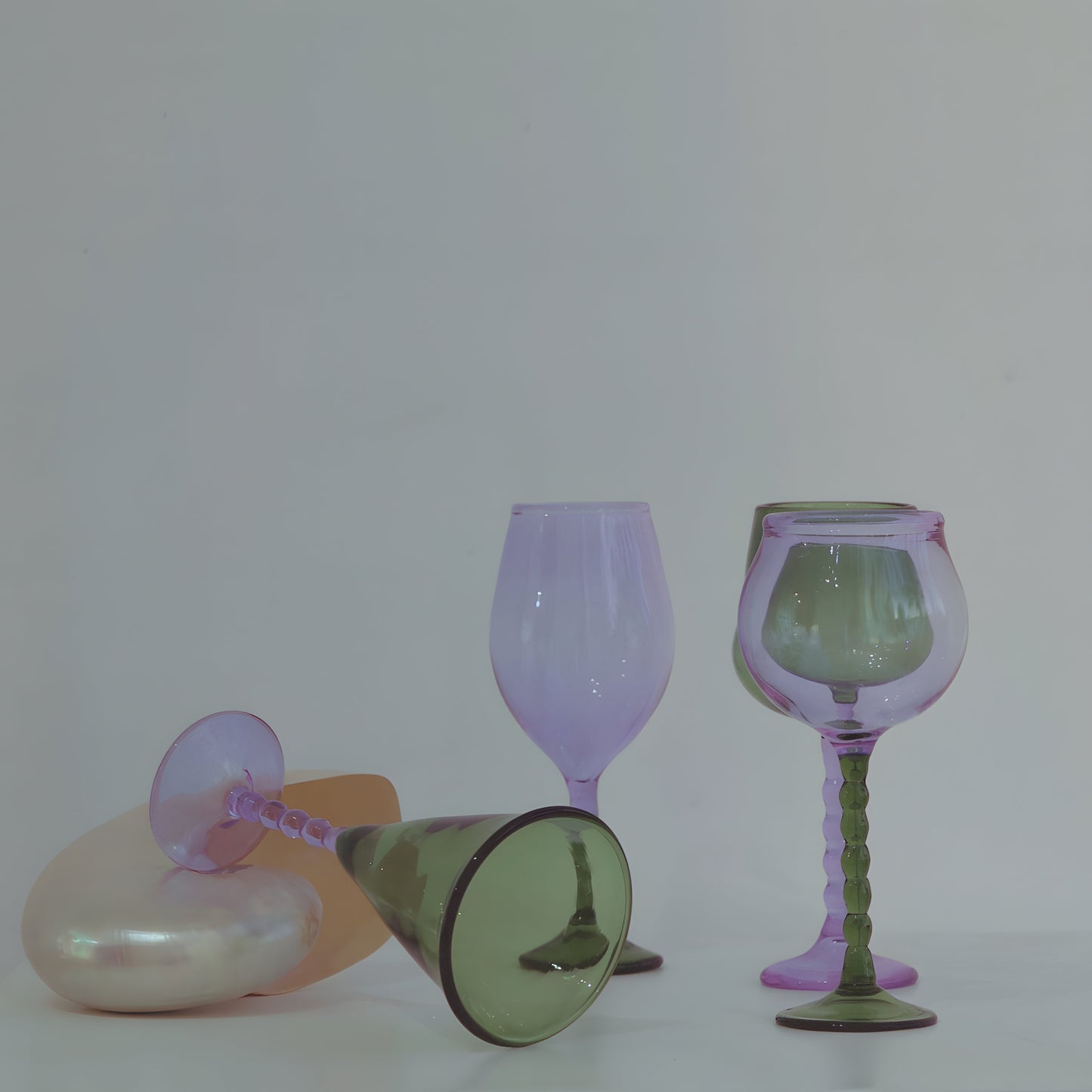 Teta Edit Liquor glasses set in soft green and lavender, elegantly arranged with one glass resting on a pearl-toned surface.