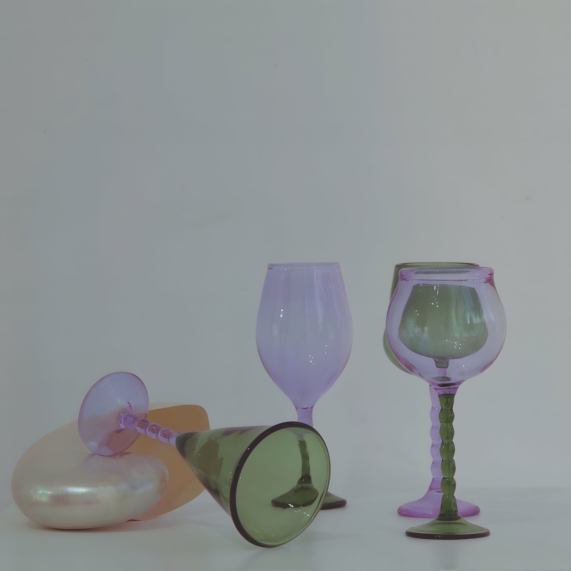 Teta Edit Liquor glasses set in soft green and lavender, elegantly arranged with one glass resting on a pearl-toned surface.
