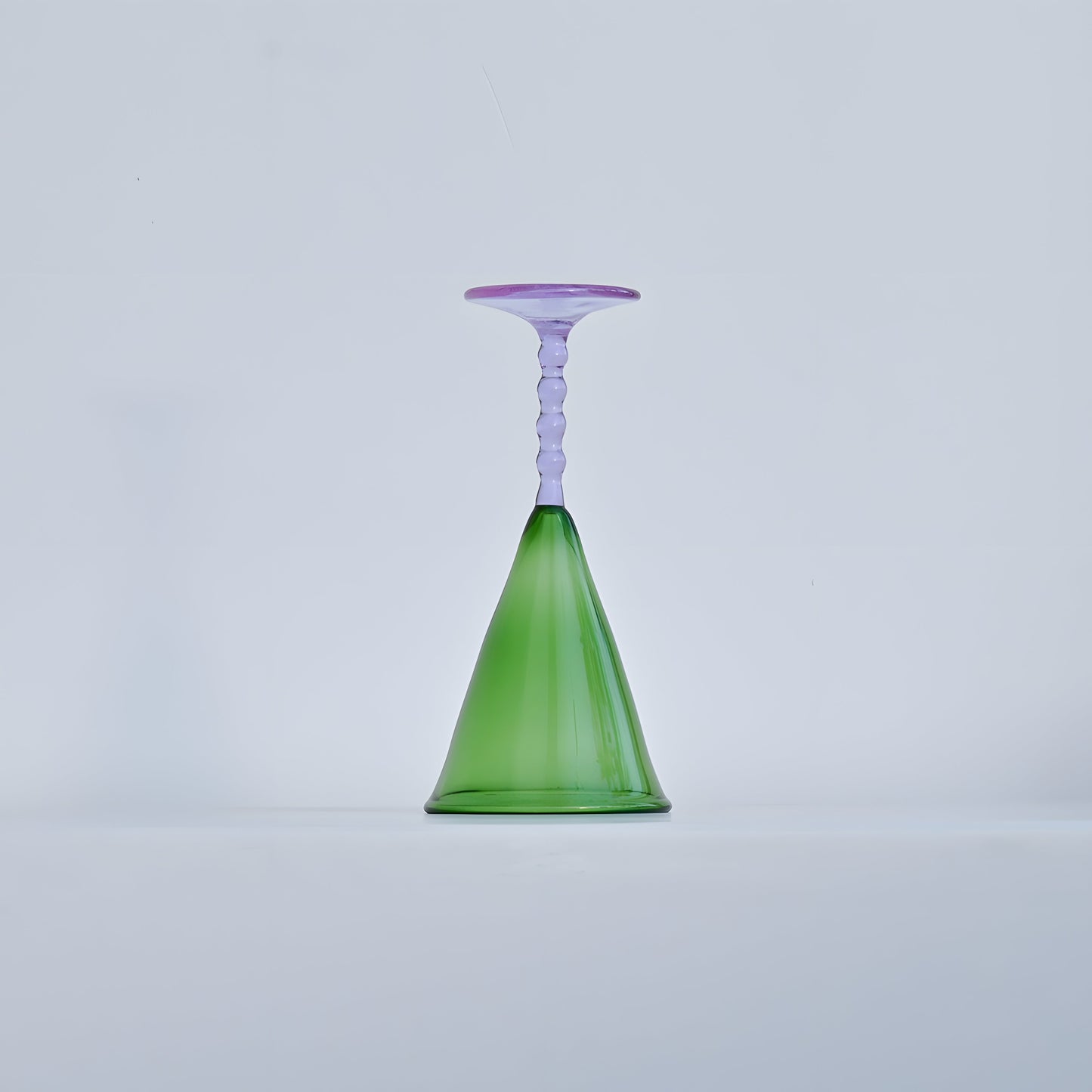 A single Teta Edit Liquor glass in green and lavender, placed upside down to highlight its unique handcrafted design.
