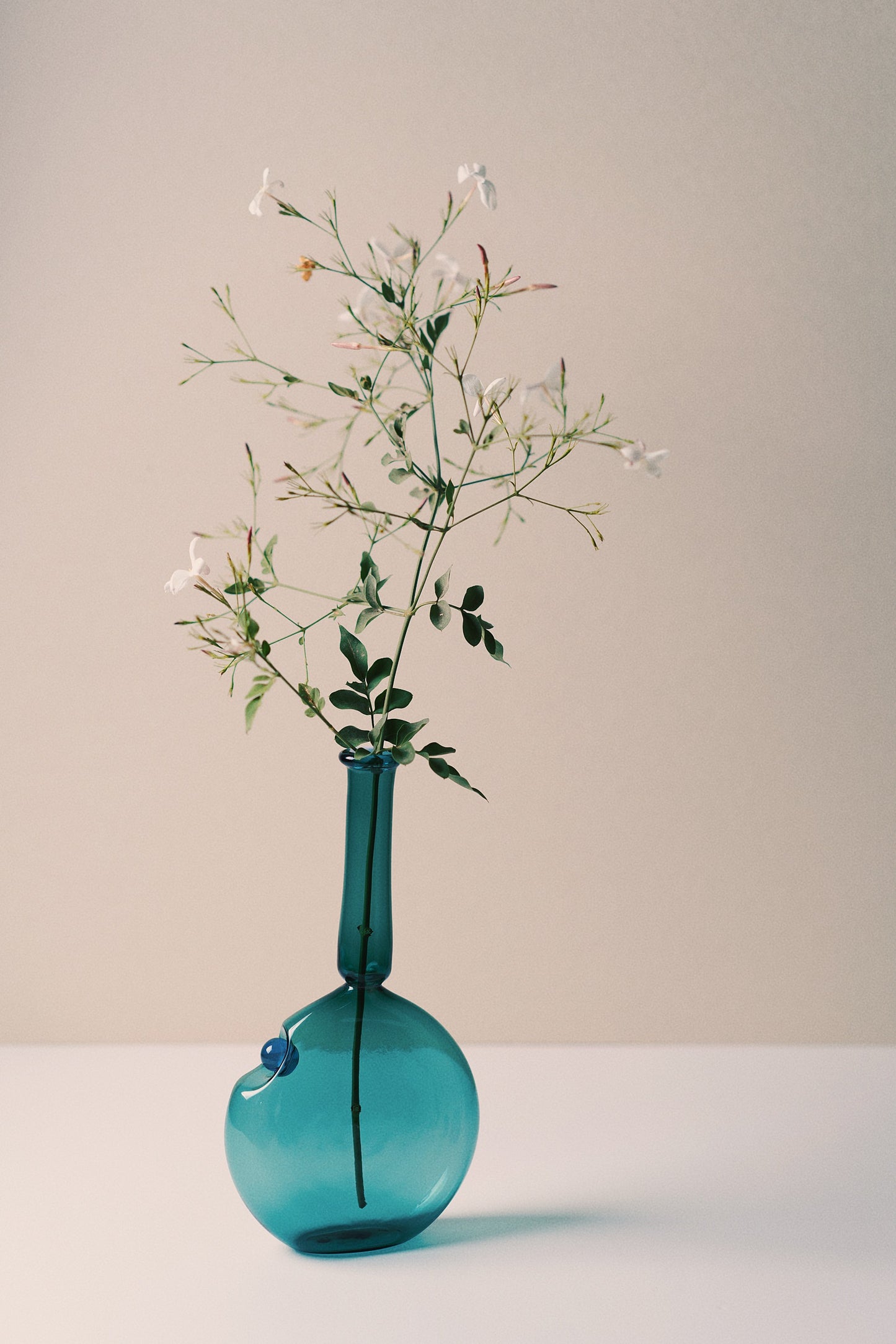 Yasmine Vase in translucent turquoise glass with a unique flask-inspired shape, holding delicate jasmine flowers. Perfect for home decor.