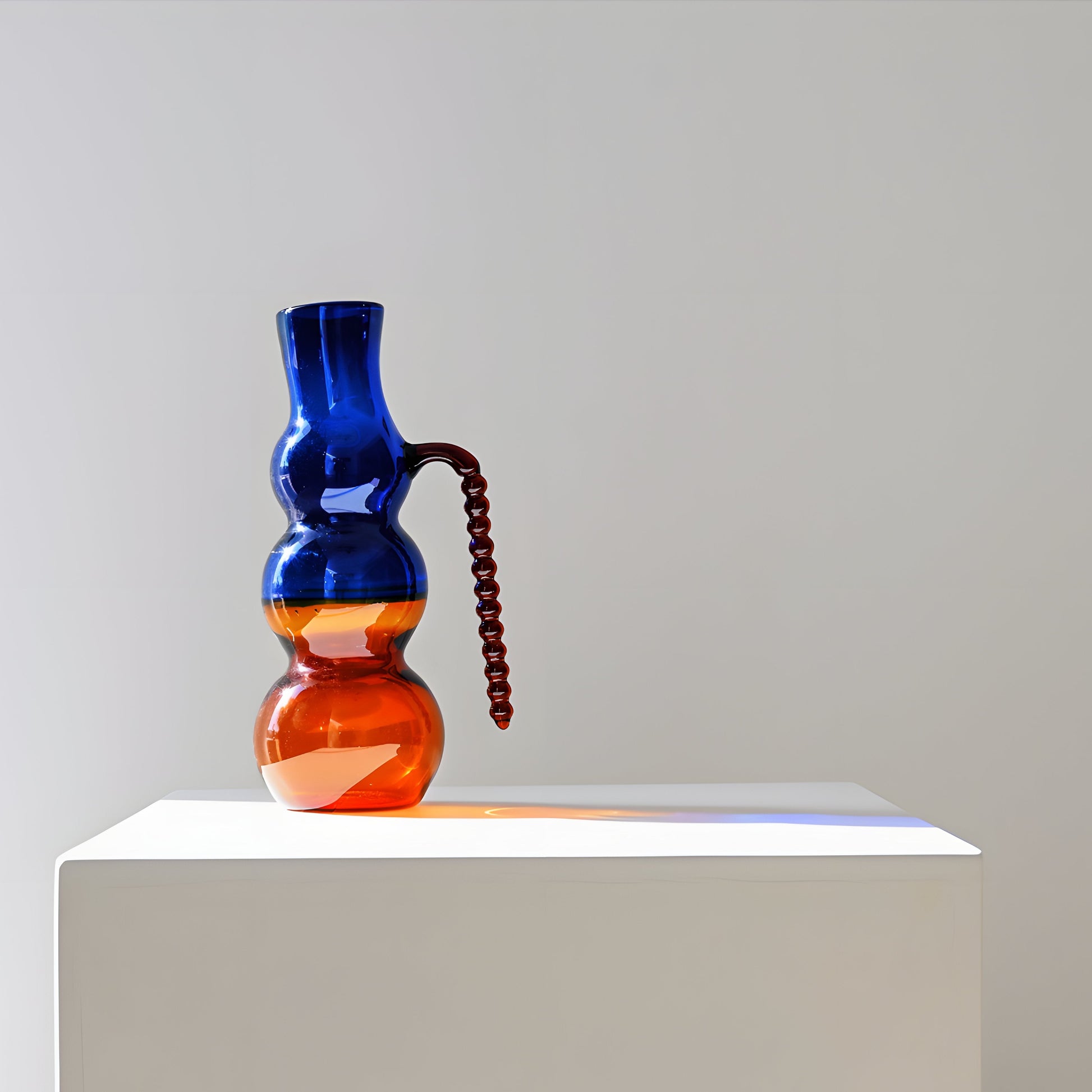 Dreamlike Pitcher:  A handcrafted glass pitcher with a whimsical silhouette, blending fluid curves and bold color contrasts. Mouth-blown by artisans, its ethereal form plays with transparency and light, adding an artful touch to any table setting.