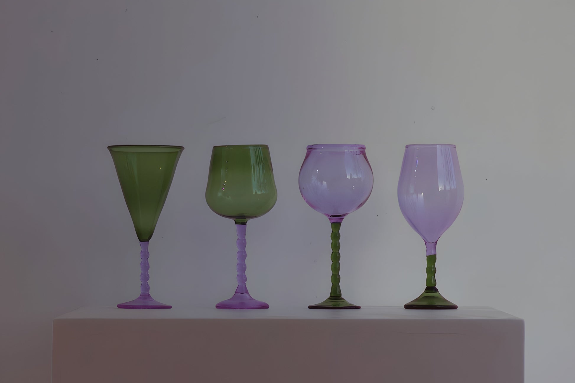 A refined Teta Edit Liquor glasses set in green and lavender, symmetrically aligned on a white pedestal for a sophisticated display.