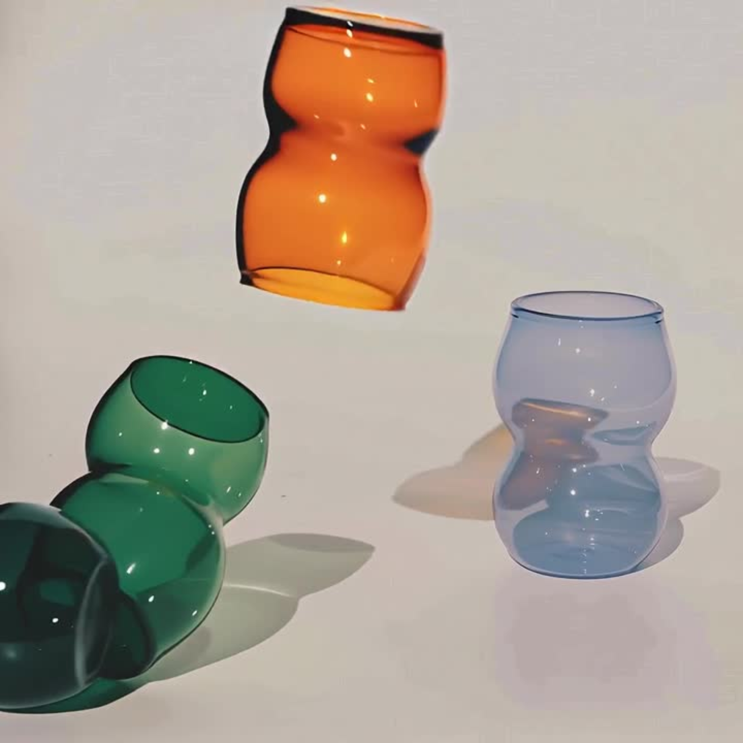 Dreamlike up Quartet cups in curvy, elegant form featuring vibrant orange, green, and translucent blue hues. Perfect for modern tableware.