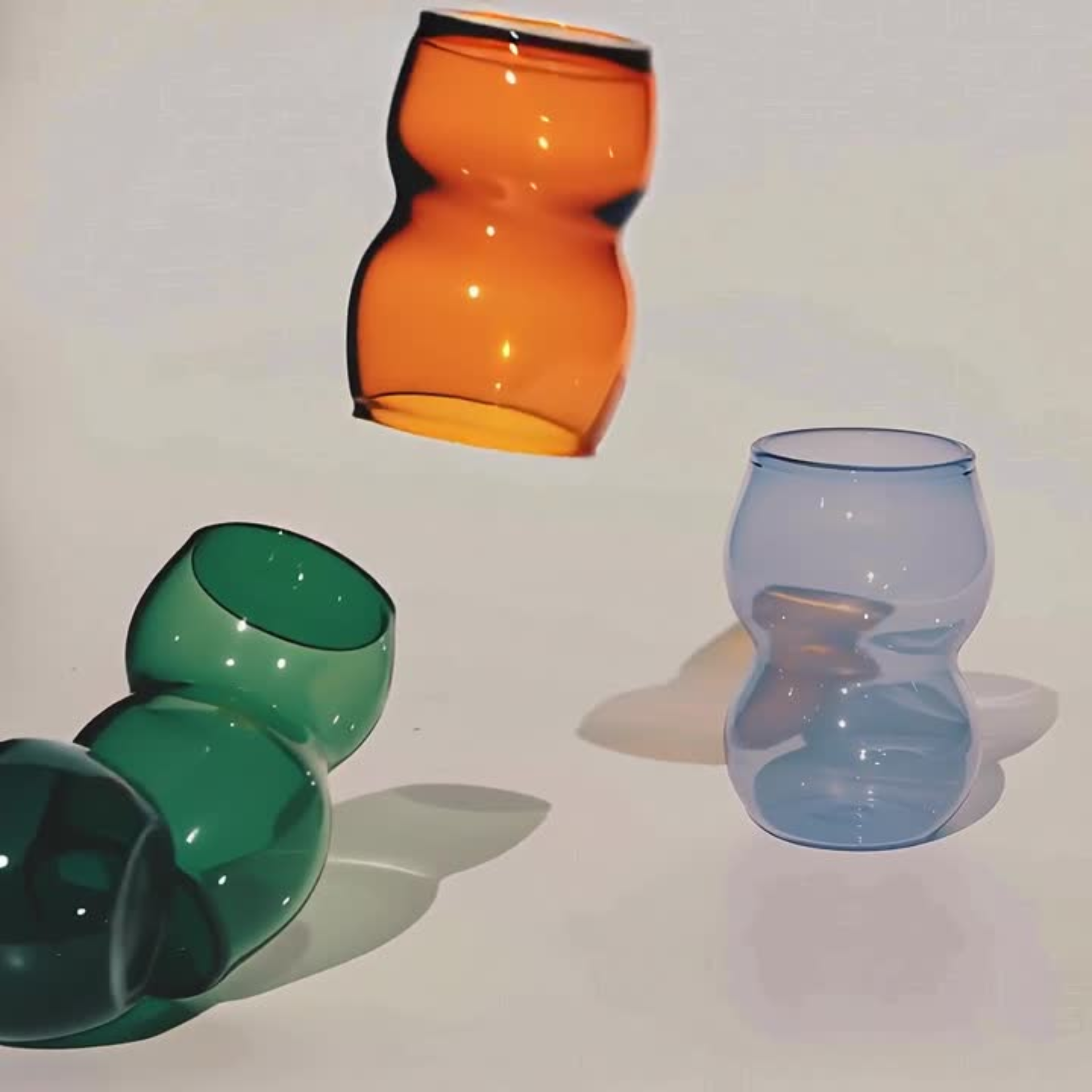 Dreamlike up Quartet cups in curvy, elegant form featuring vibrant orange, green, and translucent blue hues. Perfect for modern tableware.