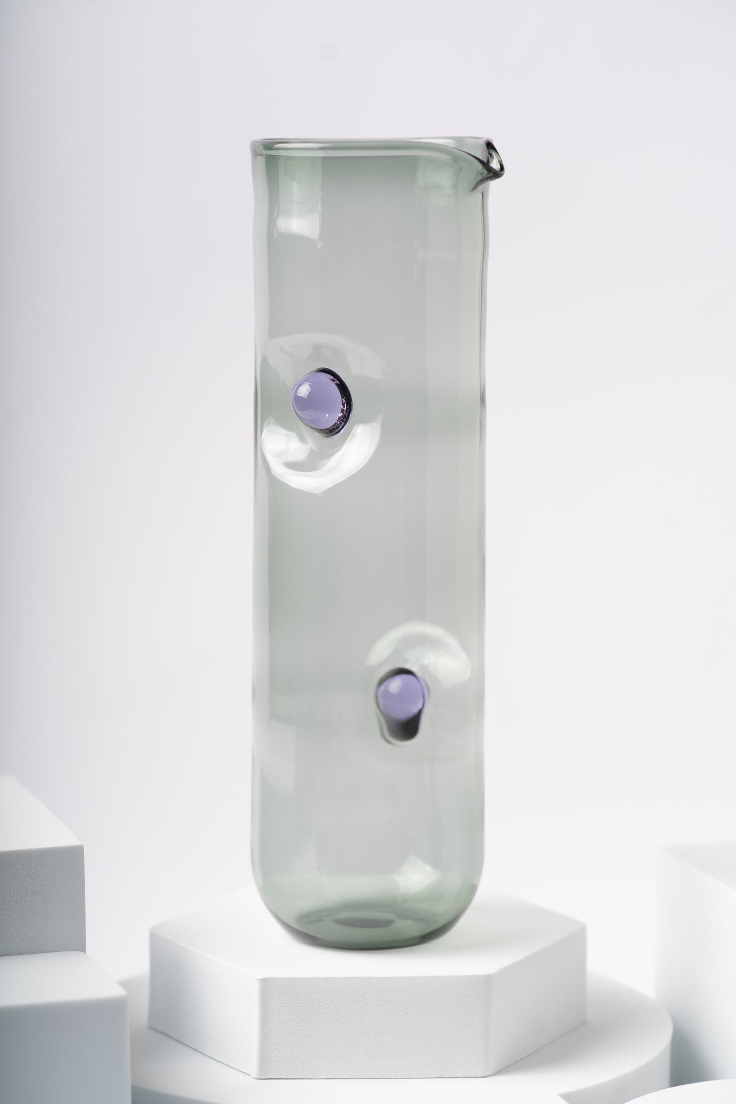 Ornamental by Lameice glass pitcher from the Eye Candy collection in a smoky gray hue with purple circular accents. Sleek and artistic serveware for drinks or floral arrangements.