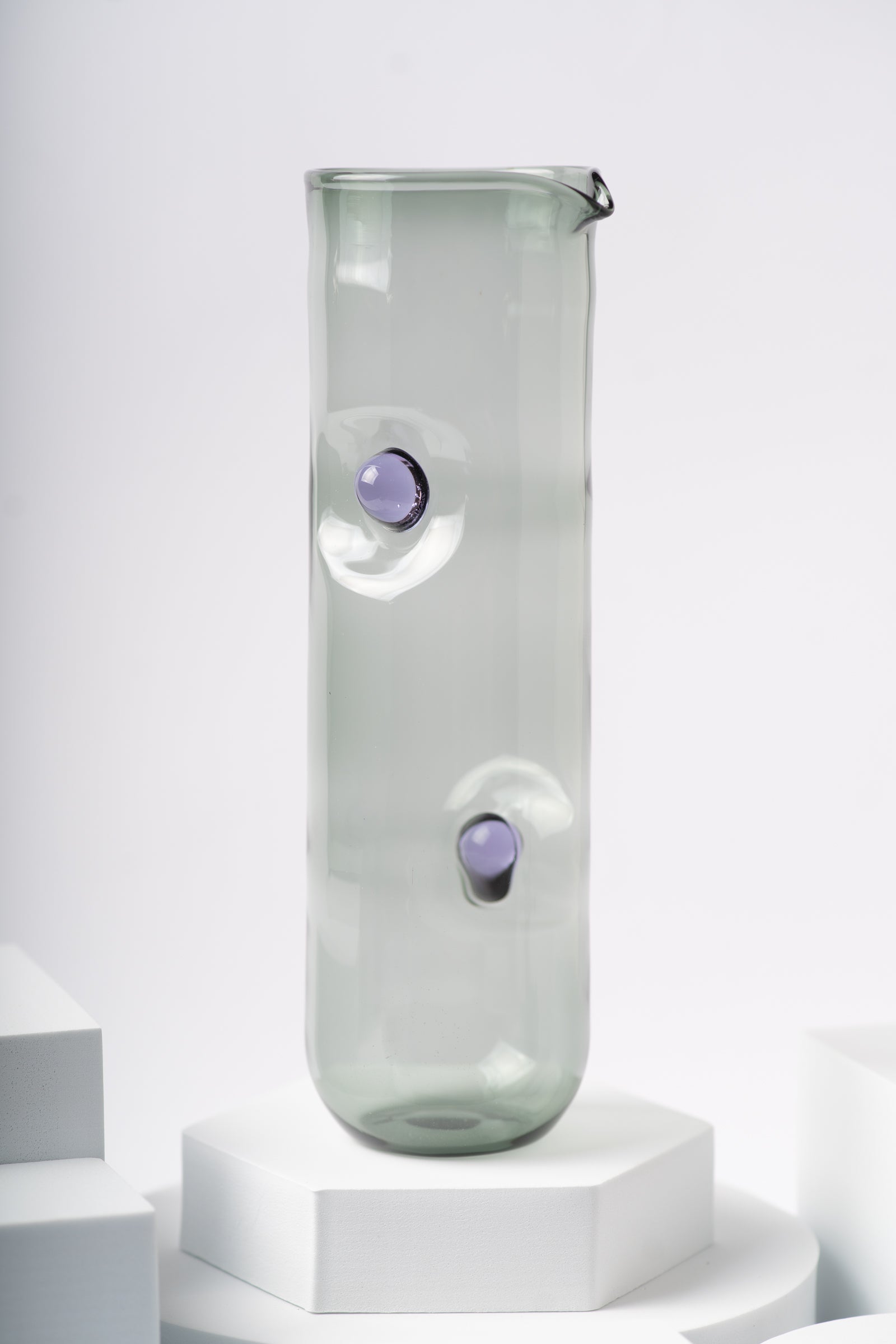 Ornamental by Lameice glass pitcher from the Eye Candy collection in a smoky gray hue with purple circular accents. Sleek and artistic serveware for drinks or floral arrangements.