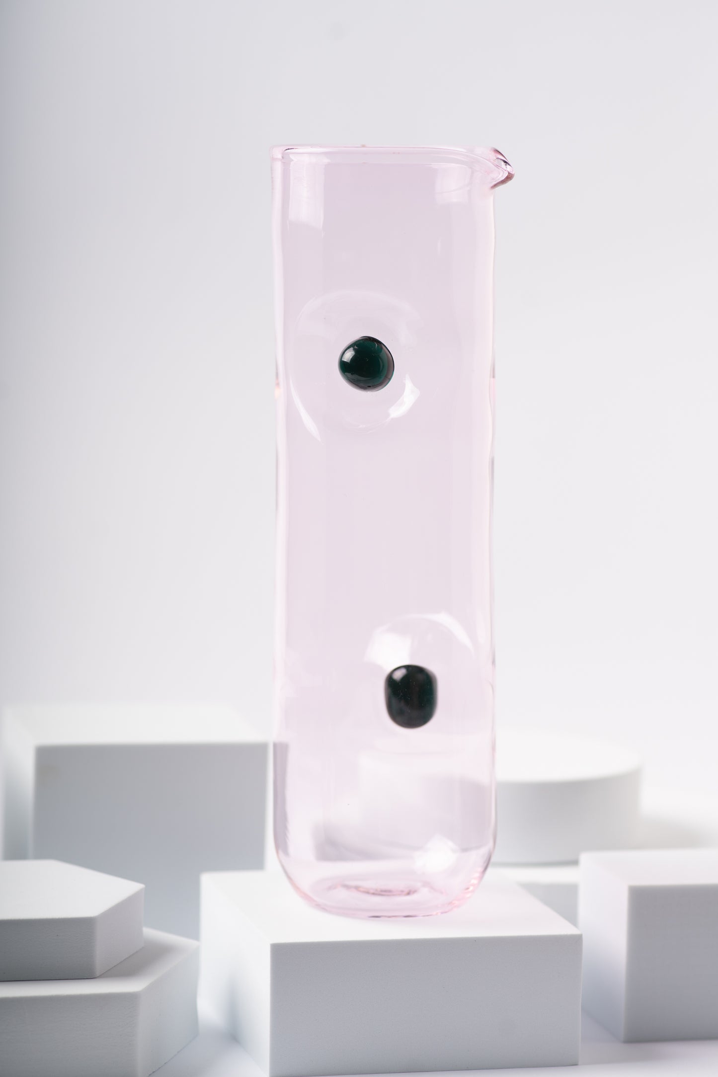 Soft pink glass pitcher from the Eye Candy collection by Ornamental by Lameice, featuring black circular accents. A delicate and artistic serveware piece for drinks or floral arrangements.