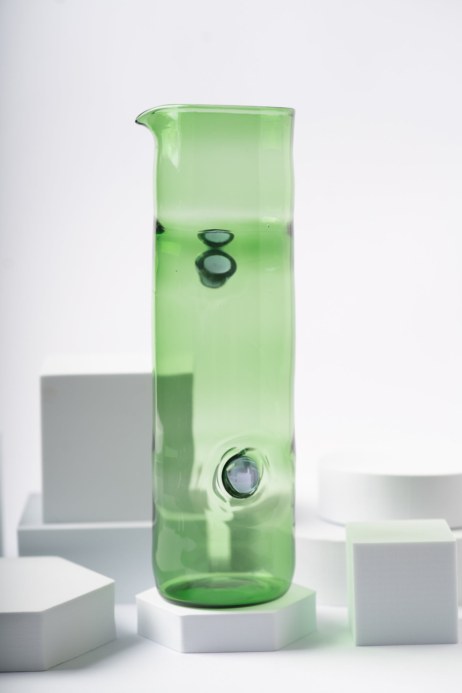 Vibrant green glass pitcher from the Eye Candy collection by Ornamental by Lameice, featuring a sleek design with black circular accents. Ideal for serving beverages or as a decorative vase.