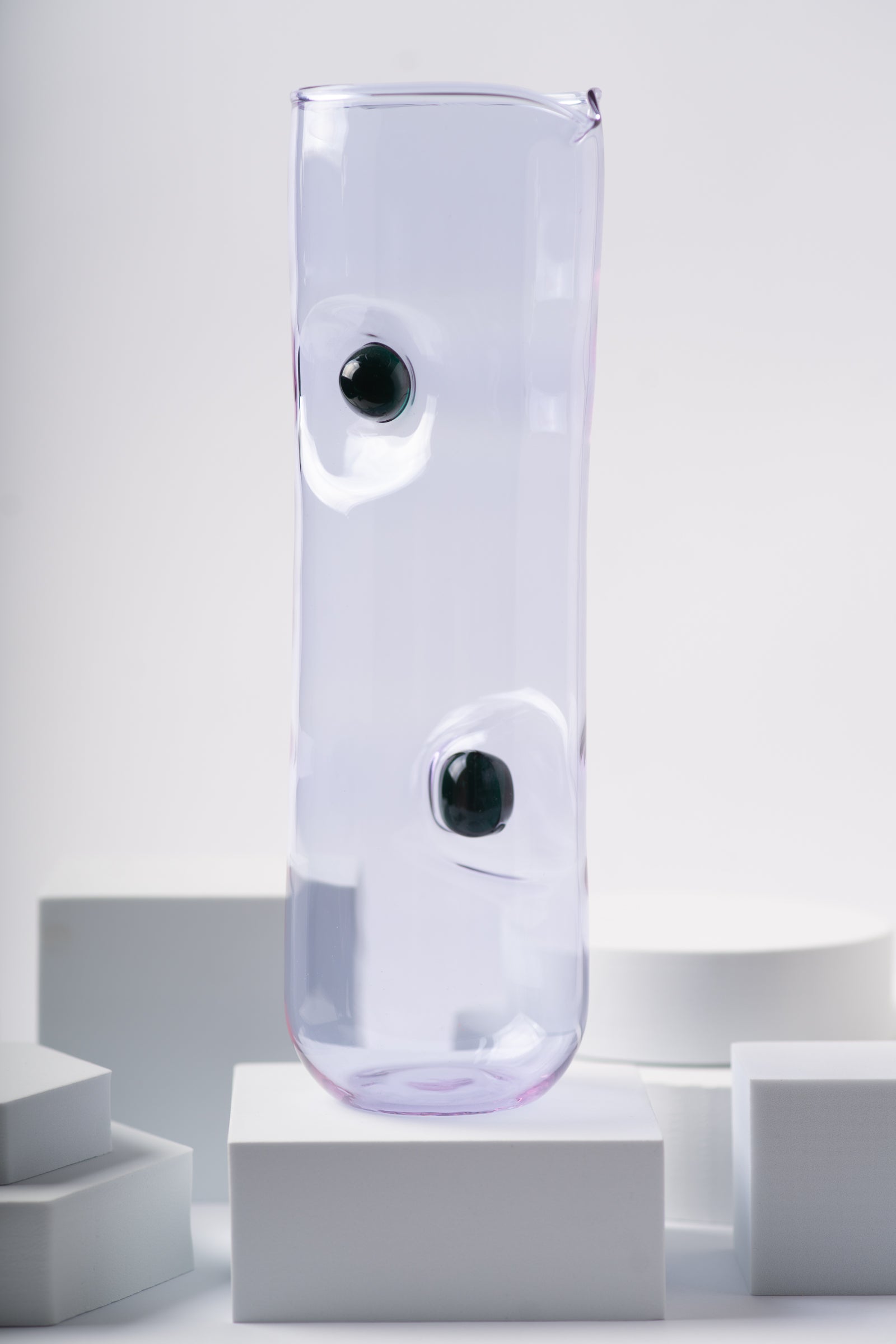 Lavender-hued glass pitcher from the Eye Candy collection by Ornamental by Lameice with black circular accents. A modern and elegant serveware piece for versatile use.