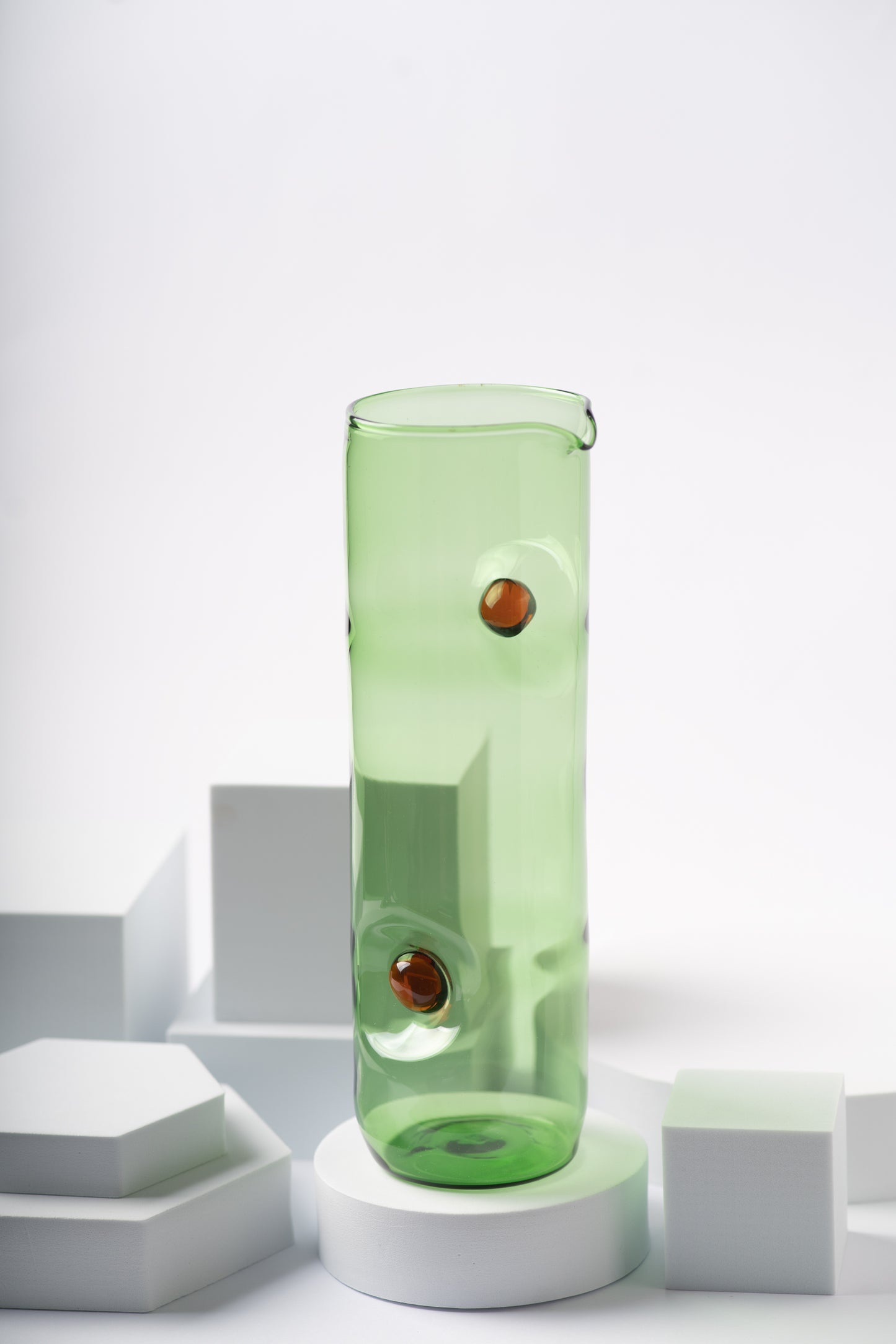 Lush green glass pitcher from the Eye Candy collection by Ornamental by Lameice, adorned with amber circular accents. A stylish and functional addition to any dining setup.